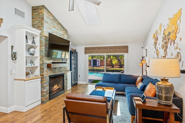 living area featuring vaulted ceiling, light wood finished floors, a skylight, a fireplace, and baseboards