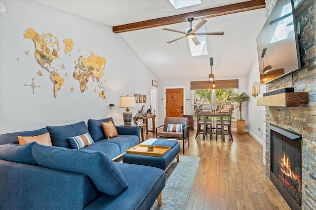 living room with a skylight, a ceiling fan, beam ceiling, light wood-type flooring, and baseboards