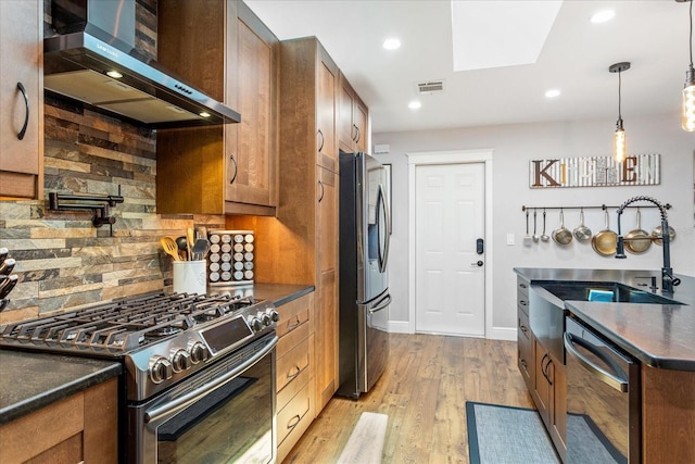 kitchen with wall chimney exhaust hood, appliances with stainless steel finishes, dark countertops, brown cabinets, and recessed lighting