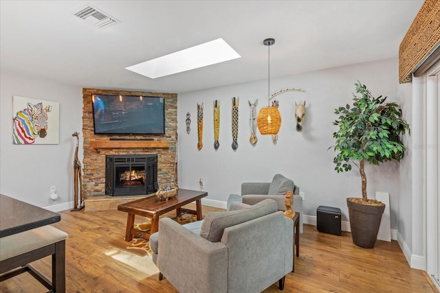 living room with a skylight, a fireplace, light wood-style flooring, and baseboards