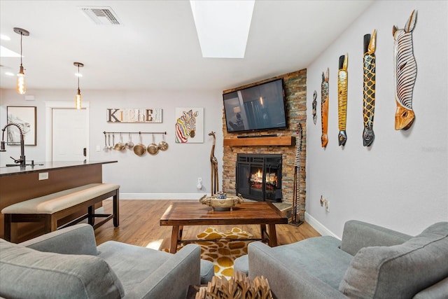living area with baseboards, light wood-style flooring, a stone fireplace, and a skylight