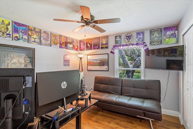 living area with ceiling fan, wood finished floors, a textured ceiling, and baseboards