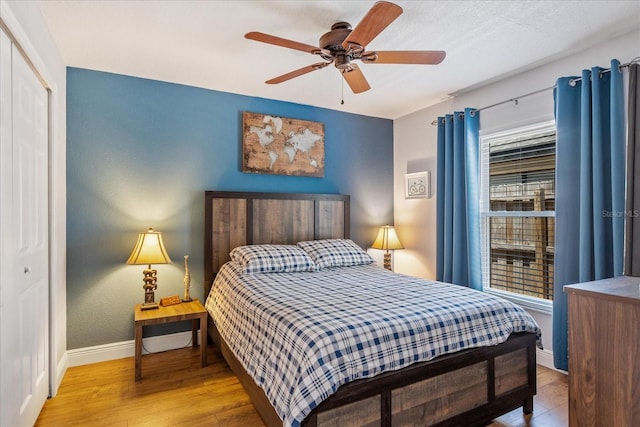 bedroom featuring baseboards, wood finished floors, a closet, and a ceiling fan
