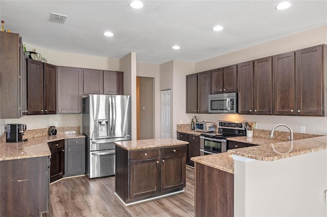 kitchen with light stone counters, dark brown cabinetry, light wood-style floors, and stainless steel appliances