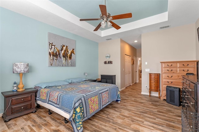bedroom with visible vents, baseboards, wood finished floors, and a raised ceiling