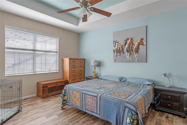bedroom with ceiling fan, a tray ceiling, baseboards, and wood finished floors