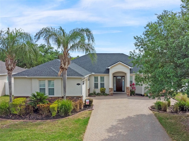 single story home featuring stucco siding, stone siding, decorative driveway, and a shingled roof