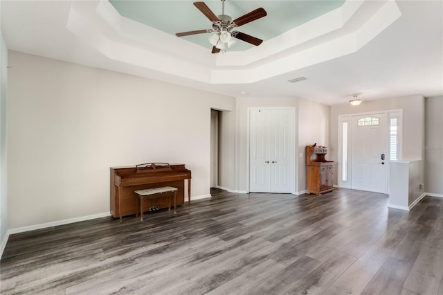 interior space with ceiling fan, a tray ceiling, visible vents, wood finished floors, and baseboards