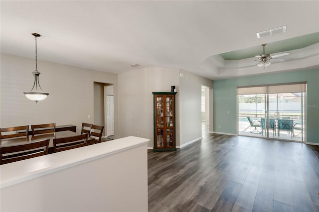 living area featuring dark wood-style flooring, baseboards, visible vents, a tray ceiling, and ceiling fan