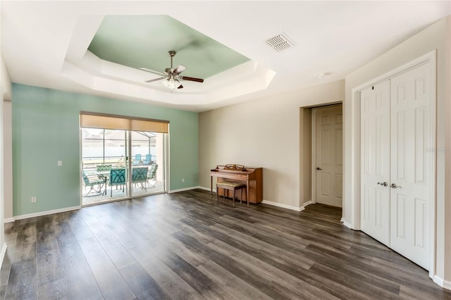 unfurnished bedroom with baseboards, dark wood-type flooring, visible vents, a tray ceiling, and access to exterior