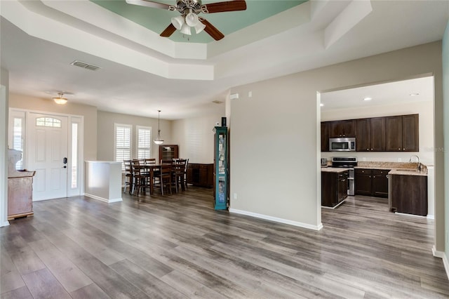 living area featuring visible vents, ceiling fan, a tray ceiling, and wood finished floors
