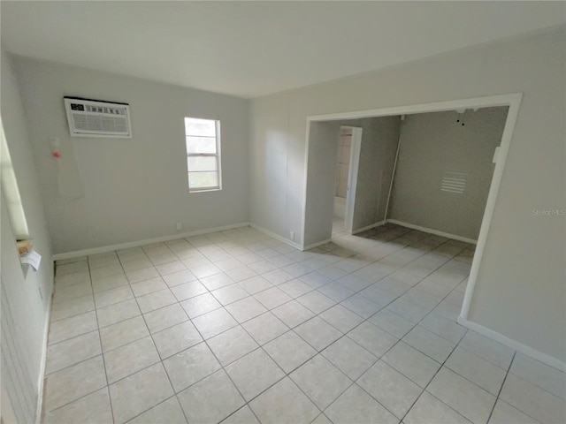 unfurnished bedroom with light tile patterned flooring, baseboards, and an AC wall unit