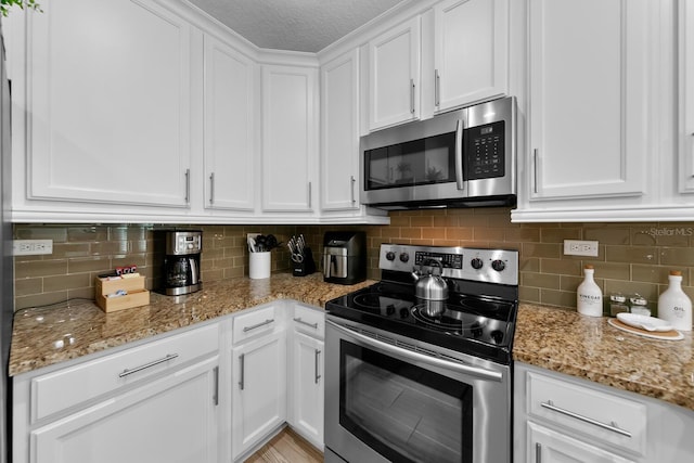 412 5th Ave S, Jacksonville Beach, FL 32250 - kitchen featuring a textured ceiling, stainless steel appliances, tasteful backsplash, white cabinetry, and light stone counters