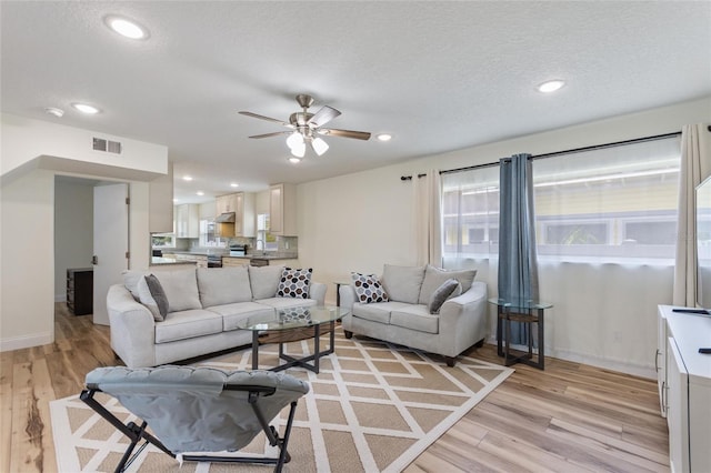 living area with a textured ceiling, visible vents, light wood finished floors, recessed lighting, and a ceiling fan