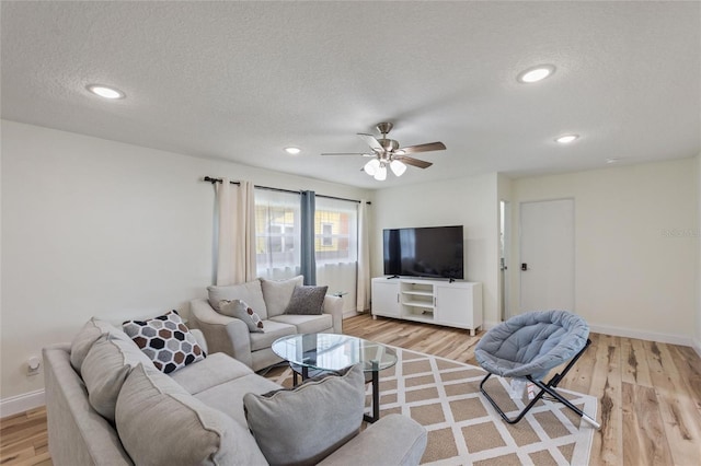 living area featuring baseboards, light wood-type flooring, ceiling fan, and a textured ceiling