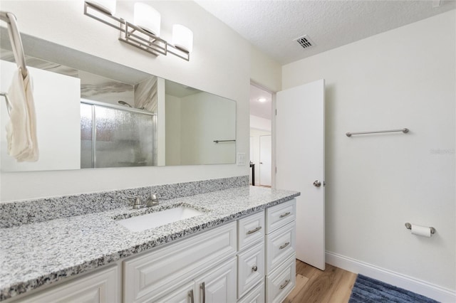 bathroom featuring vanity, a textured ceiling, a stall shower, visible vents, and wood finished floors