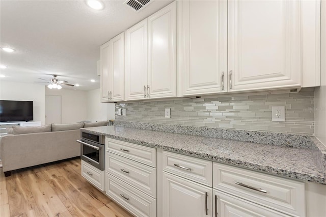 kitchen featuring white cabinets, visible vents, light wood finished floors, oven, and a ceiling fan