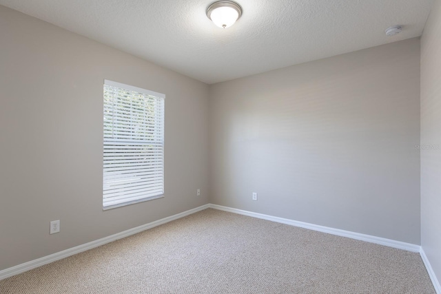 spare room with light carpet, baseboards, and a textured ceiling
