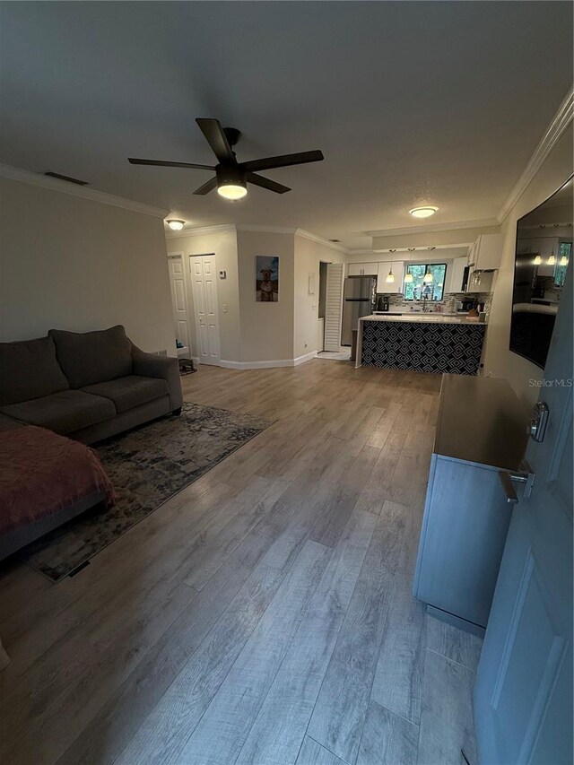 living area featuring a ceiling fan, ornamental molding, and light wood finished floors