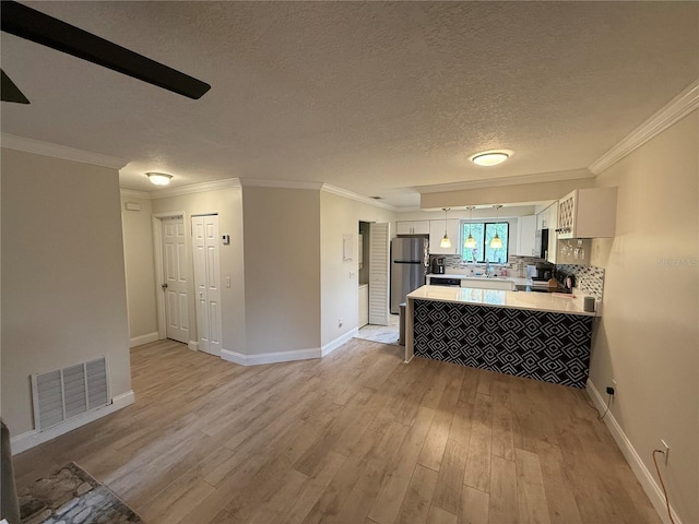 kitchen featuring light wood finished floors, visible vents, freestanding refrigerator, white cabinets, and a peninsula