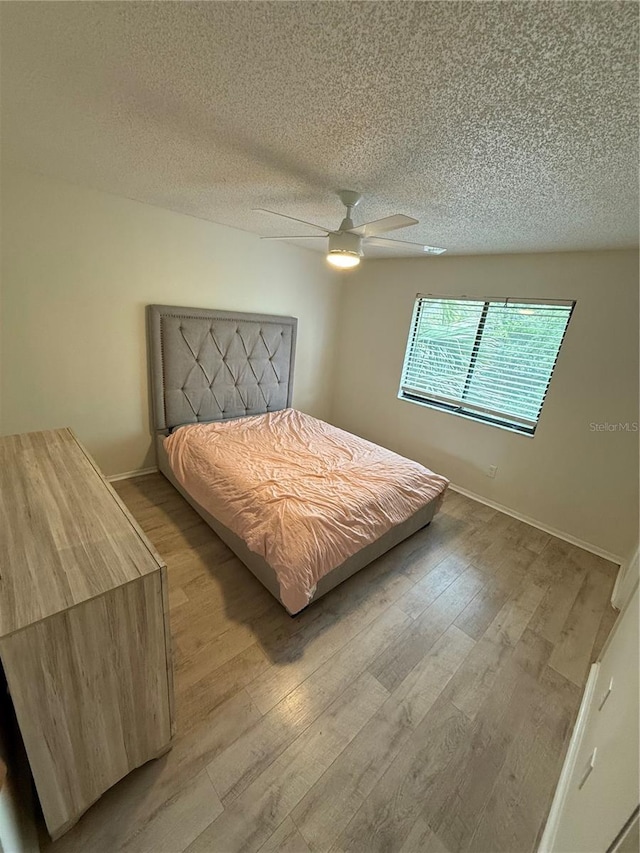 bedroom featuring baseboards, wood finished floors, ceiling fan, and a textured ceiling