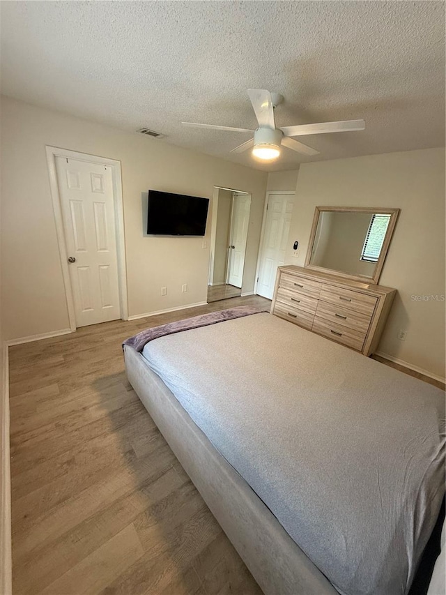 bedroom with baseboards, visible vents, a textured ceiling, and wood finished floors