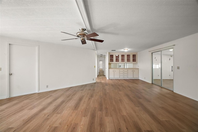 unfurnished living room with wood finished floors, a textured ceiling, baseboards, and ceiling fan