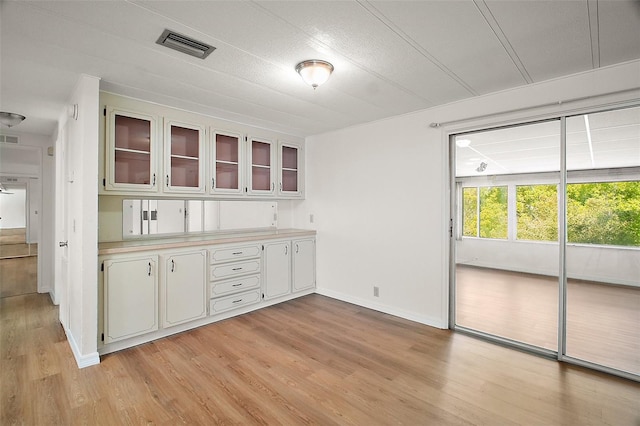 kitchen featuring light countertops, visible vents, white cabinets, glass insert cabinets, and light wood-style floors