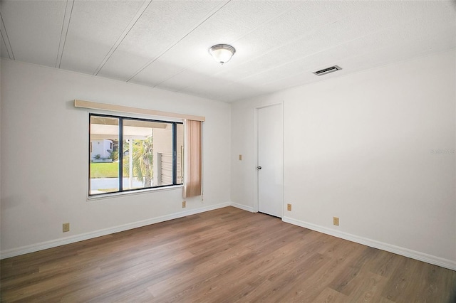 empty room with baseboards, visible vents, wood finished floors, and a textured ceiling