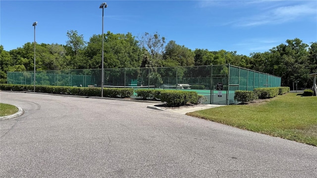 view of tennis court featuring fence and a yard