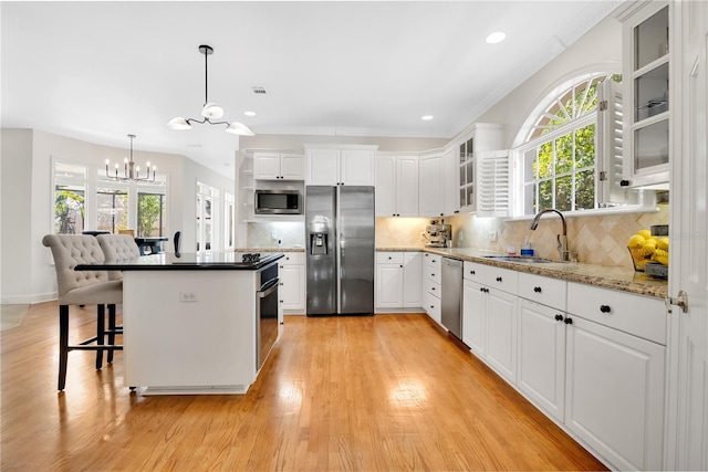 1560 Woodland Ave, Winter Park, FL 32789 - kitchen with a sink, stainless steel appliances, white cabinets, light wood-style floors, and an inviting chandelier