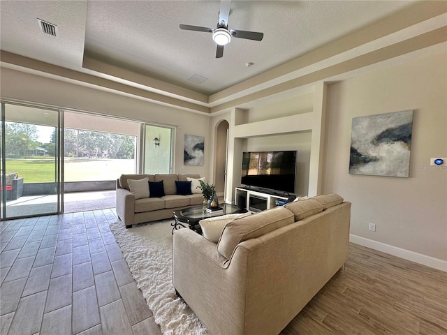 living area featuring a ceiling fan, wood finished floors, a textured ceiling, arched walkways, and baseboards