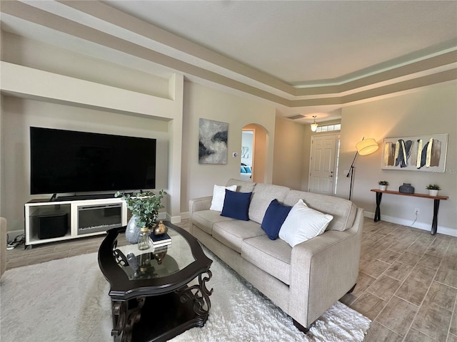 living room featuring arched walkways, a raised ceiling, wood finished floors, and baseboards