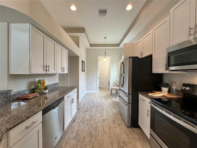 kitchen with light wood finished floors, dark stone countertops, a raised ceiling, visible vents, and appliances with stainless steel finishes