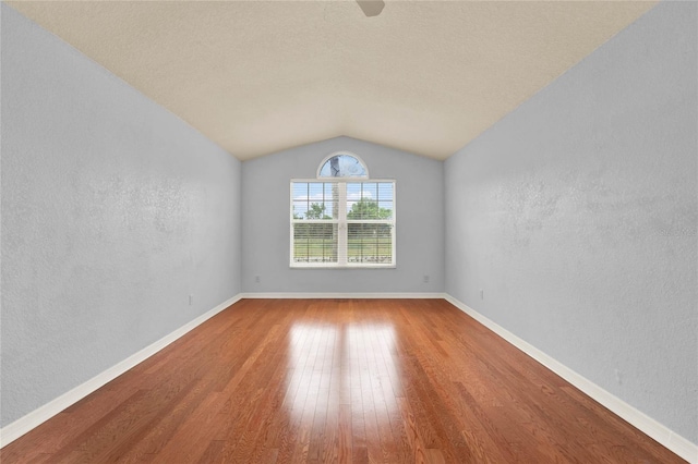 unfurnished room featuring baseboards, lofted ceiling, a textured wall, and wood finished floors