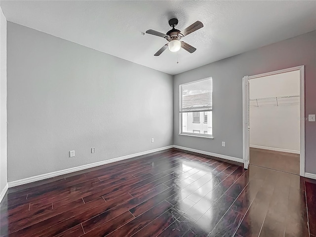 unfurnished room with baseboards, ceiling fan, a textured ceiling, and dark wood-style flooring