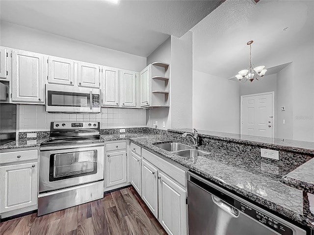 kitchen featuring dark stone counters, a chandelier, stainless steel appliances, open shelves, and a sink