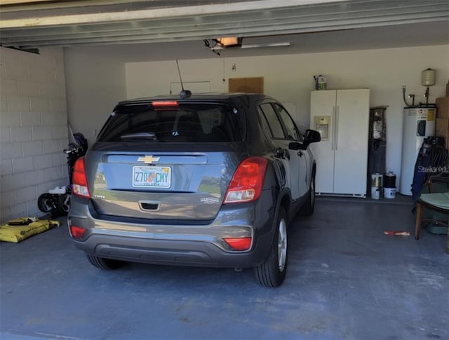 garage featuring water heater, concrete block wall, white refrigerator with ice dispenser, and a garage door opener