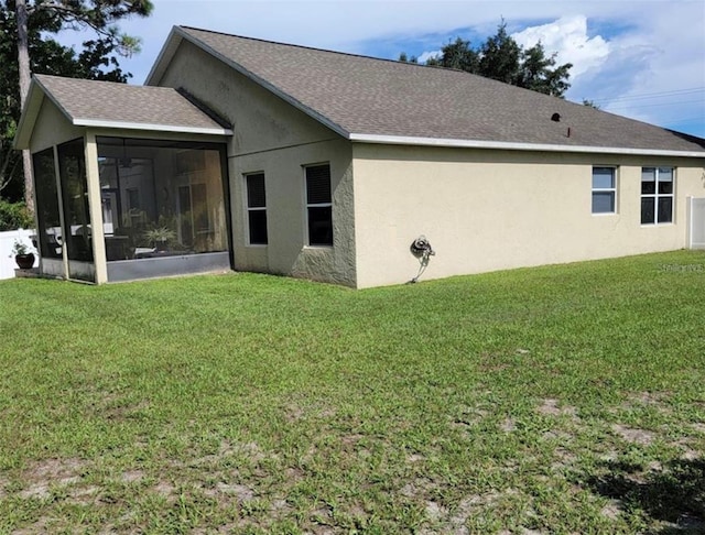 rear view of property with a lawn, stucco siding, a sunroom, and roof with shingles