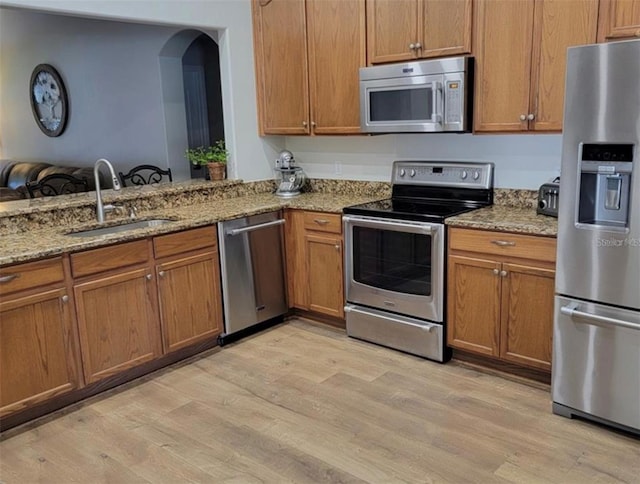 kitchen featuring a sink, light wood finished floors, light stone countertops, brown cabinets, and stainless steel appliances