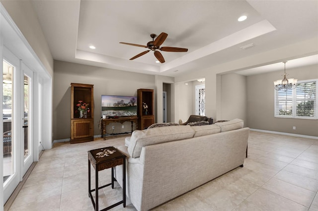 living area with baseboards, light tile patterned floors, ceiling fan with notable chandelier, and a tray ceiling