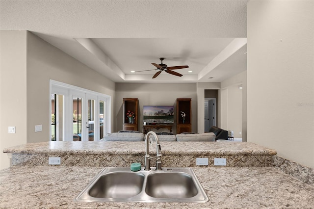 kitchen with a sink, a raised ceiling, ceiling fan, recessed lighting, and french doors