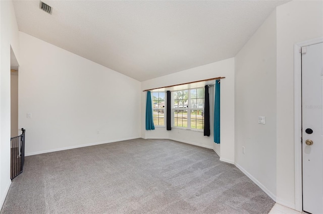 empty room with vaulted ceiling, light carpet, a textured ceiling, baseboards, and visible vents