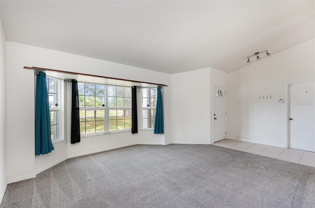 tiled empty room with rail lighting, carpet flooring, lofted ceiling, and a healthy amount of sunlight