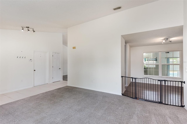 carpeted empty room with vaulted ceiling, a textured ceiling, tile patterned floors, visible vents, and track lighting