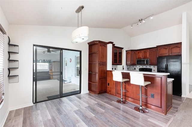 kitchen featuring vaulted ceiling, light countertops, black fridge, a peninsula, and stainless steel microwave