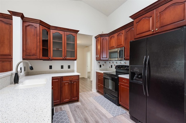 kitchen featuring lofted ceiling, black appliances, light countertops, and a sink