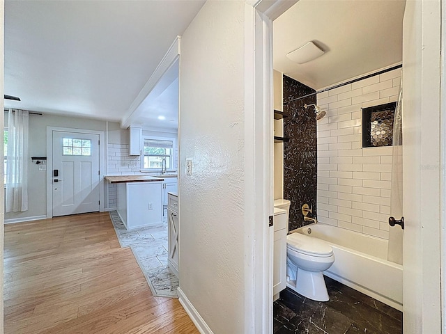 1121 49th Ave N, Saint Petersburg, FL 33703 - full bath featuring decorative backsplash, baseboards, toilet, wood finished floors, and shower / tub combination