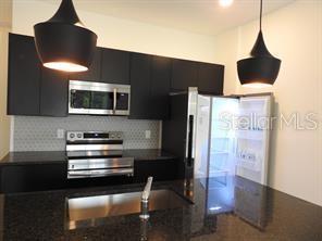 3296 Tranquil Trl, Kissimmee, FL 34747 - kitchen featuring appliances with stainless steel finishes, dark cabinets, decorative backsplash, pendant lighting, and a sink