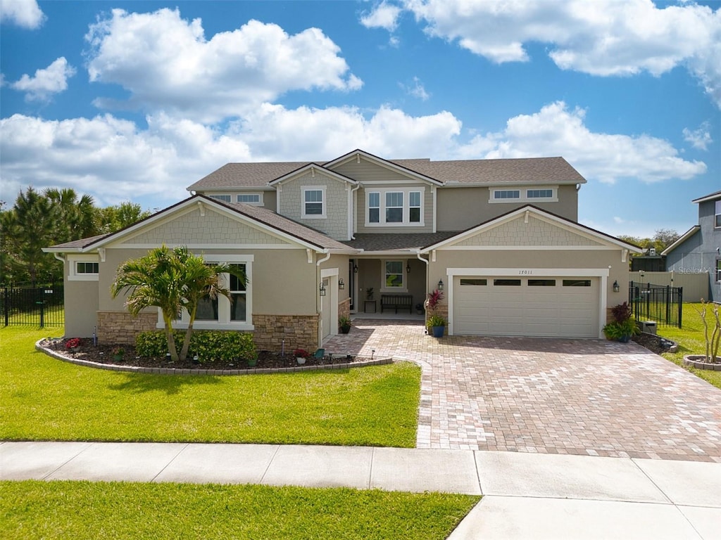 craftsman house with decorative driveway, a front yard, fence, stone siding, and an attached garage